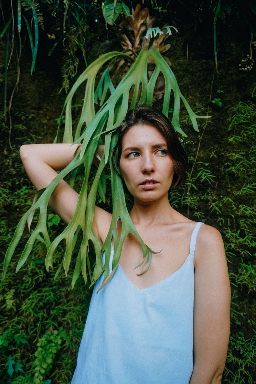 woman in blue tank top standing near a green plant
